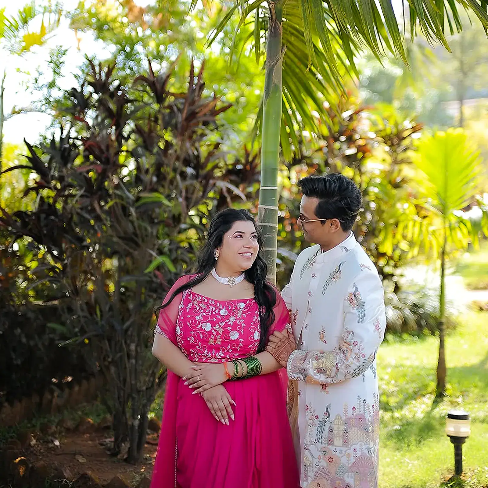The couple standing close among the palms, smiling at each other