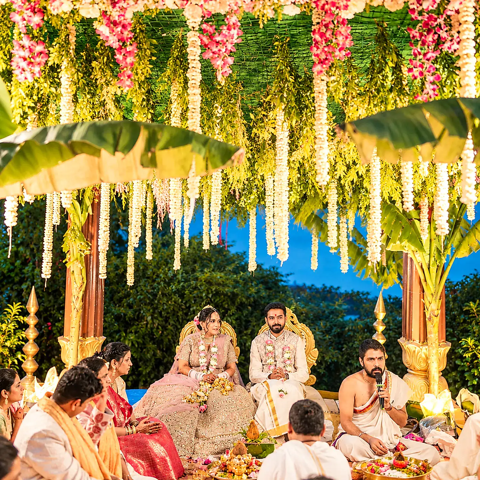 The couple seated for the pheras beneath a floral mandap with family around