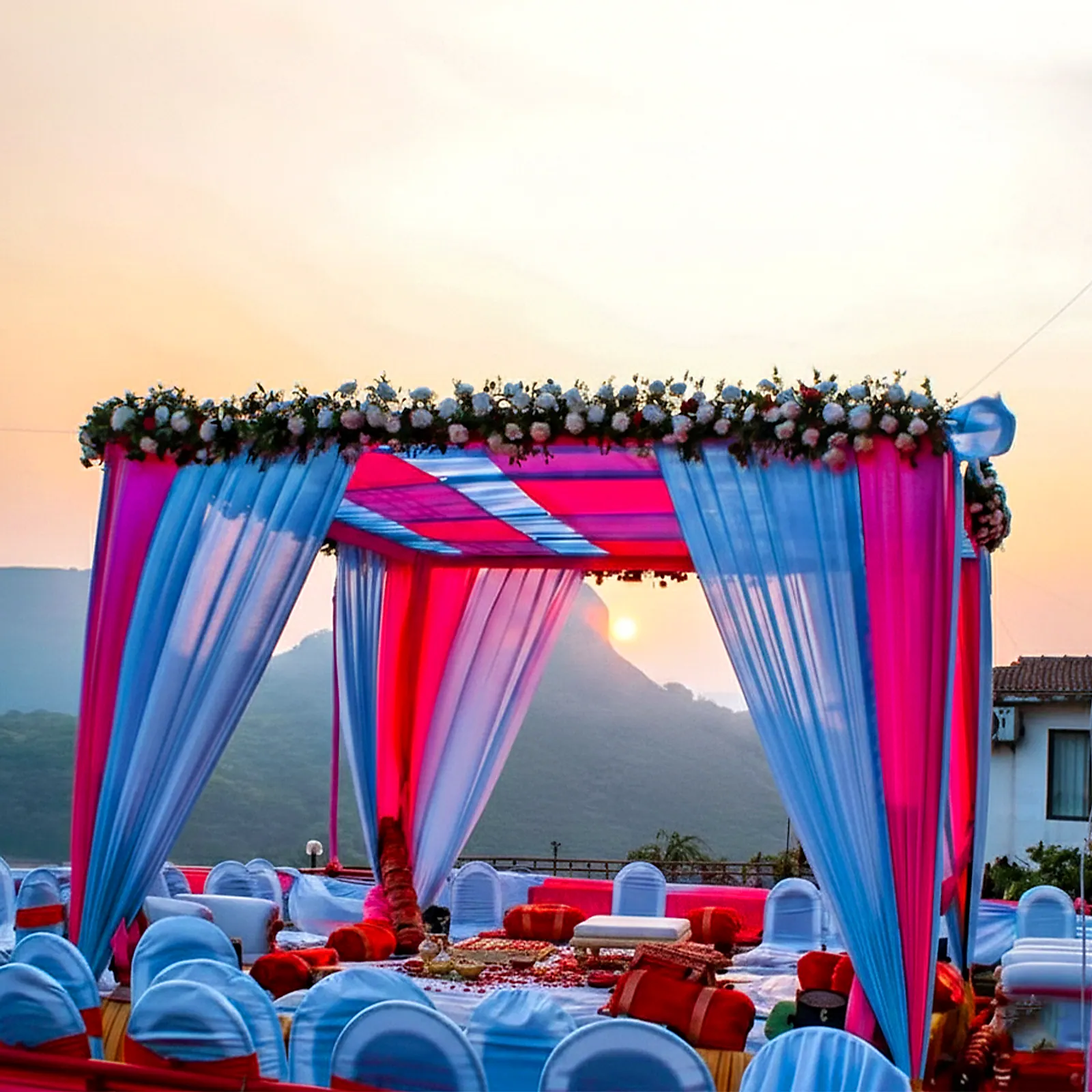 A floral mandap on the lawn at sunset, the Sahyadri hills behind