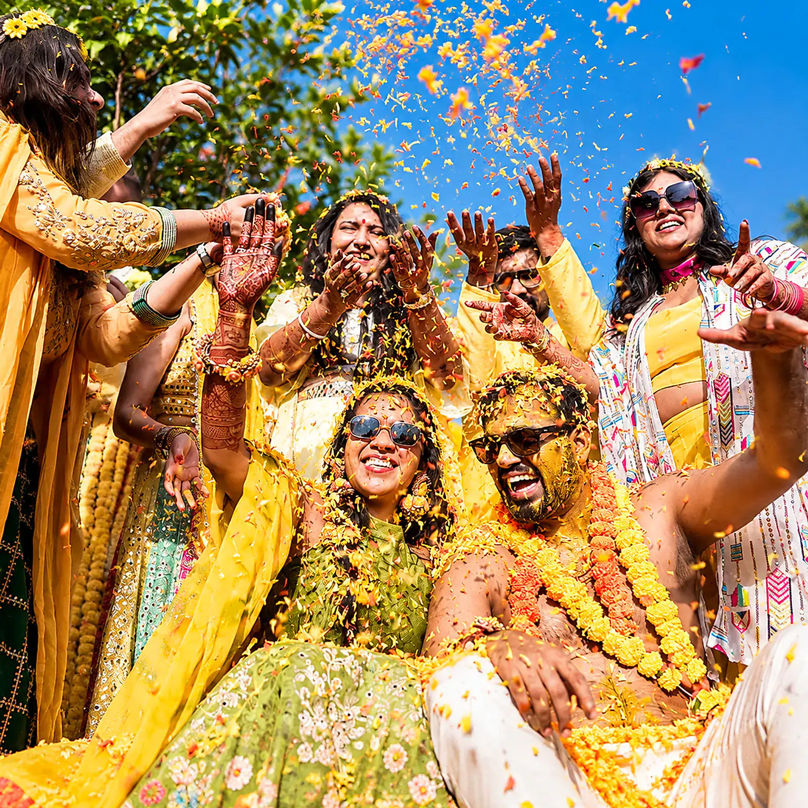 Friends in yellow laughing and throwing marigold petals during the haldi