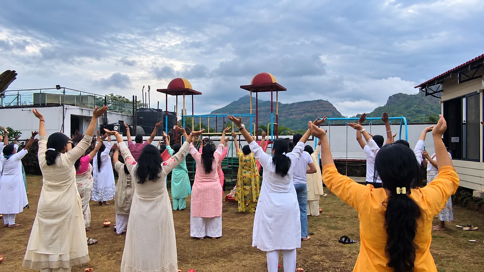 A group stretching together on the lawn with the Sahyadri hills behind